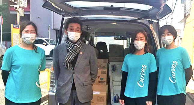 荷物を積んだ車の前で4人の従業員が並んでいます。
