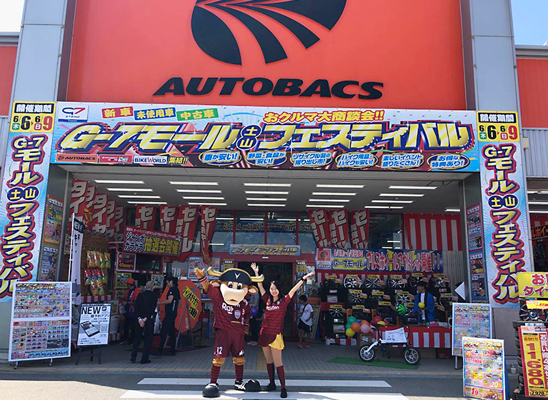 オートバックス店舗前でマスコットのモーヴィと女性がポーズをとっている