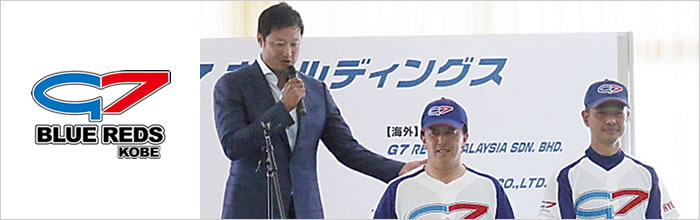 監督がマイクを持っており2名の選手が正面を向いています。