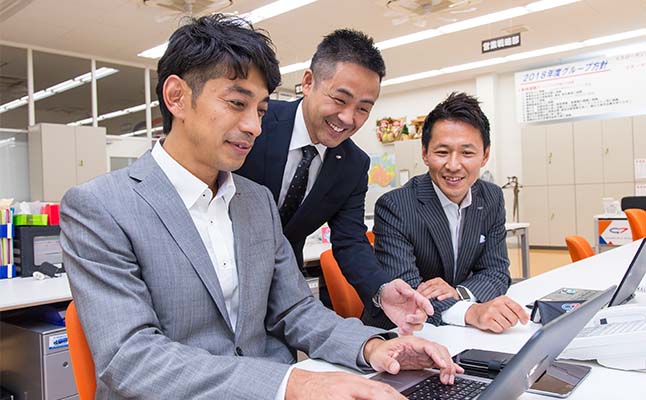 社内の様子-3人の従業員がパソコン画面を見ながら話し合っている