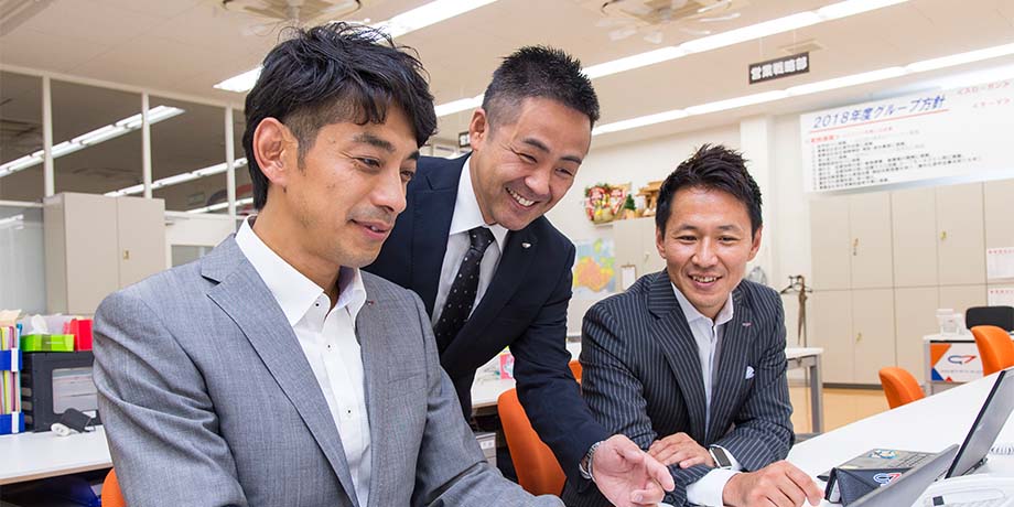 社内の様子-3人の従業員がパソコン画面を見ながら話し合っている